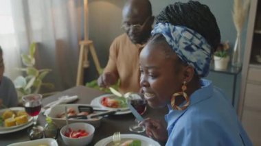 Evde tatilde yemek yerken, başörtüsü takmış gülümseyen ve aile üyeleriyle sohbet eden Afro-Amerikan kadınlarının seçici odak noktası.