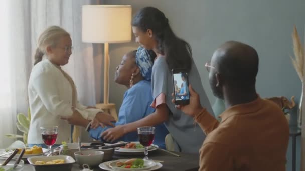 アフリカ系アメリカ人男性 スマートフォンを持って 幸せな妻と2人の娘のビデオを撮影 自宅で休日の夕食中に楽しんでいます — ストック動画