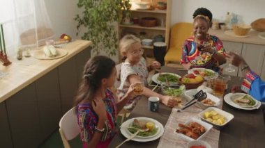 Geleneksel Dashiki kıyafetleriyle kadehleri tostlarla tokuştururken Kwanza bayramında şenlikli bir akşam yemeği yerken yüksek açılı yavaş çekim yapan mutlu Afrikalı Amerikalı aile.