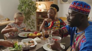 Afrika kökenli Amerikalı bir adam dashiki ve kufi şapka takıp ailesiyle yemek yerken aynı zamanda Kwanzaa 'da tatilde birlikte yemek yiyor.