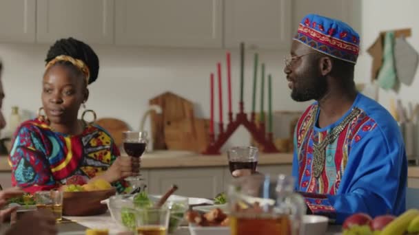 アフリカ系アメリカ人の妻と夫 伝統的なダシキのチュニックでトーストでメガネを飲んで 赤ワインを飲んで クワンザの夕食で子供たちと話をする — ストック動画