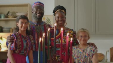 Evde Kwanzaa kutlamalarında Kinara mumlarının arkasında gülümseyen ve poz veren neşeli Afrikalı Amerikalı aile portresi.