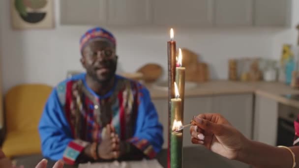 クワンザの休日の自宅のお祝いの間に家族が手を叩いている間 キナラろうそくを照らす黒人女性の手の選択的な焦点ショット — ストック動画