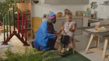 Dashiki ceketli ve kufi şapkalı Afrikalı bir babanın küçük kızına evde Kwanzaa Tatili 'nde nasıl djembe davul çalacağını öğretirken.