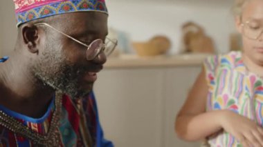 Dashiki kaftan ve kufi şapkalı neşeli Afrikalı Amerikalı babanın, kızı Kwanzaa 'nın evinde djembe davul çalarken el çırpışlarını yakından çek.