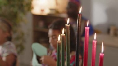 Kinara 'nın seçmeli odak noktası evde Kwanzaa tatilinde yanan yedi mum, arka planda el sanatları yapan Afro-Amerikan ailesi.