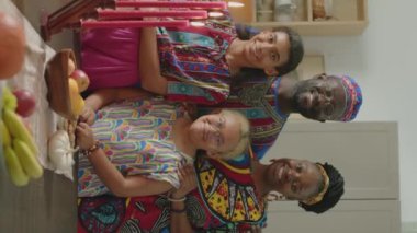 Dashiki kaftanları giyen, Kinara mumlarının arkasında kameraya gülümseyen ve poz veren neşeli Afro-Amerikan bir aile fotoğrafı.