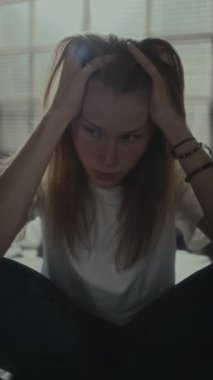 Depresyondaki kızın evde oturup saçını çekerken anksiyete ve stres yaşadığı dikey bir fotoğraf.