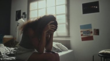 Üzgün Afrikalı Amerikalı kız telefonda mesajlar okuyor, hayal kırıklığına uğruyor ve evde elleri yatak odasında oturuyor.