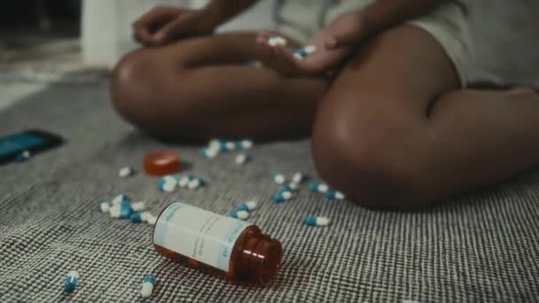 一握りの錠剤で自宅で床に座っている認識できない黒人の少女のクロップショットでズーム サイバーいじめ 自殺未遂の概念によるうつ病 — ストック動画