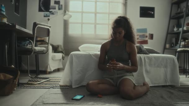 アフリカ系アメリカ人のティーンガールは スマートフォンで床に座って サイバー乱暴に苦しんでいる間 丸薬の過剰摂取で自殺するつもりです — ストック動画