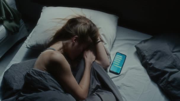 一个自上而下的镜头 一个紧张的女孩躺在手机旁边 屏幕上放着短信 她因网络欺凌而感到压力 — 图库视频影像