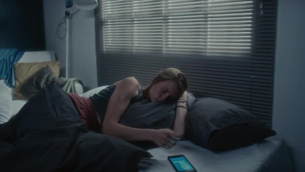 夜にベッドに横たわる若い女性 スマートフォンで恥ずかしいメッセージを読み 枕を抱き 泣いている — ストック動画