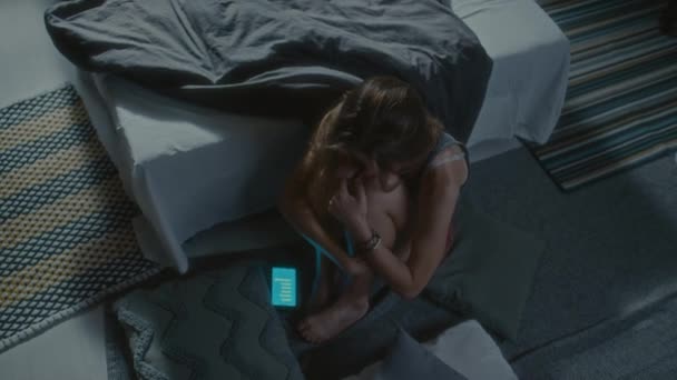 上至下拍摄的沮丧少女夜晚抱着膝盖坐在卧室的地板上 在手机上的短信中被欺负 — 图库视频影像