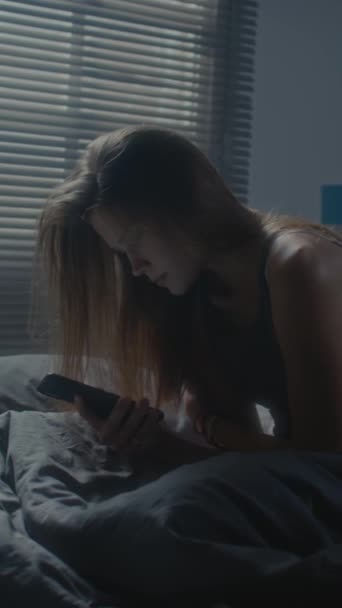 一个紧张的女孩躺在床上 检查手机 沉思地看着旁边的垂直镜头 — 图库视频影像