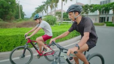 Erkek ve genç oğlu spor kıyafetleri ve kasklar takıyor bisiklet sürüyor ve dışarıda konuşuyor.