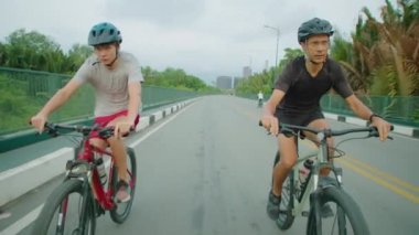 Açık havada zaman geçirirken yolda bisiklet süren sportif baba ve oğulun kasklı çekimleri.