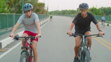 Koruyucu kasklı atletik baba ve oğul yaz günü dışarıda spor yaparken yolda bisiklet sürüyorlar.