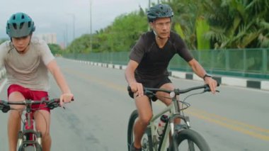 Aktif baba ve oğulun kaskları ve spor kıyafetleri içinde dışarıda bisiklet sürüşünün ön görüntüsü.