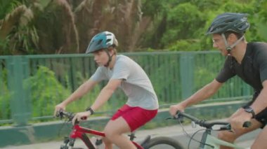 Korumalı kask takan bir adam ve oğlu yaz günü dışarıda bisiklet sürerler.