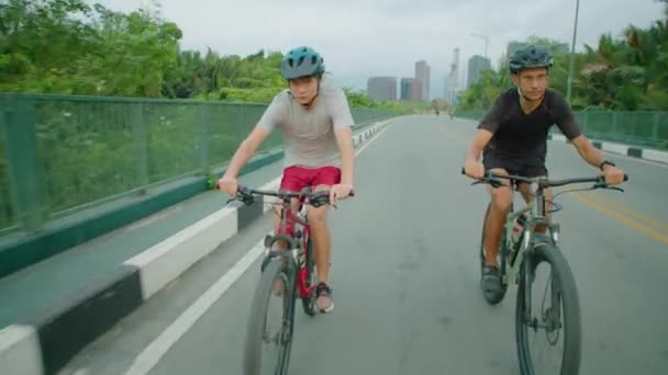 在沥青路面上 穿着防护头盔和运动服骑自行车的小男孩和他的父亲的前景 — 图库视频影像