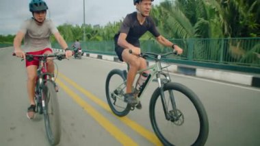 Yaz günü bisikletle seyahat ederken kask ve spor kıyafetlerle gezen genç çocuk ve babasının görüntülerini yukarı kaldır.