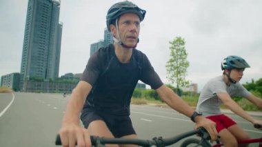 Yol boyunca bisiklet sürerken giysili ve kasklı baba genç oğluyla konuşuyor.