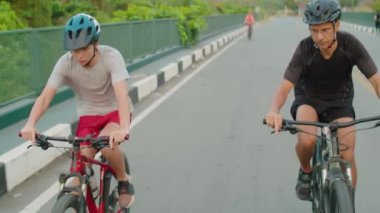 Baba ve oğul koruyucu miğferler ve spor kıyafetleriyle yaz günü bisiklet sürerken yolda bisiklet sürerler.