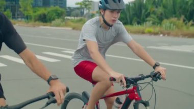 Kasklı sportif baba ve oğul şehirde kaldırımlı yolda bisikletle gidiyorlar.