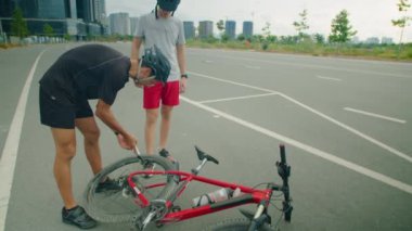 Baba ve oğlunun koruyucu kaskları ve spor kıyafetleri içinde bisiklet lastiklerini şişirmek için bisiklet pompası kullanırken.