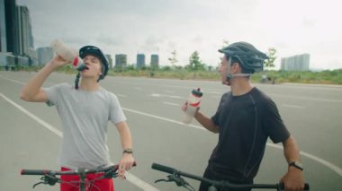 Baba ve oğlunun yolda bisikletle dikilirken, su molası verirken ve konuşurken çekilen görüntüleri.