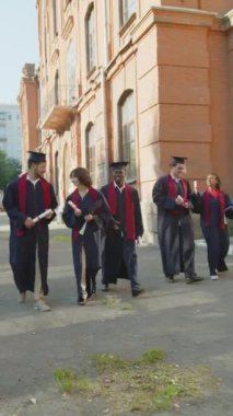 Bir yerlere giden ve birbirleriyle konuşan çok ırklı mutlu mezunların dikey görüntüsü.