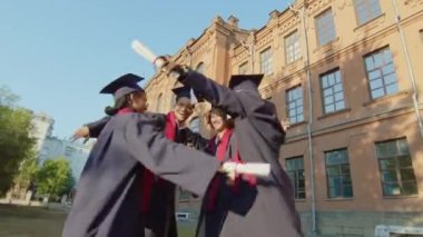 Dışarıda diploma aldıktan sonra birbirine sarılan, cüppeli ve şapkalı üniversiteli gençlerin bakış açısı düşük.