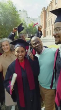 Mezuniyet töreninde, öğrenci şapkalı ve cüppeli arkadaşlarının okul arkadaşları ve aileleriyle selfie çekerken.