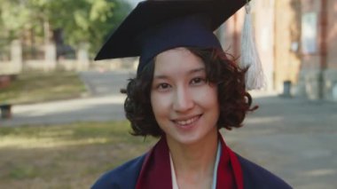 Şapkalı ve cüppeli genç kız öğrencinin dışarıda kameraya bakarken yakın portresi.