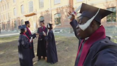 Siyahi bir adamın, üniversite arkadaşlarıyla cübbe ve şapkalarla selfie çekerken çekilmiş görüntüsü.