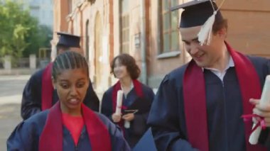 Mezuniyet töreninden sonra bir yere giderken iletişim kuran orta boy mutlu öğrenciler.