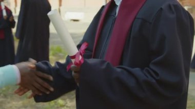 Orta yaşlı Afrikalı bir adamın üniversiteden mezun olurken oğluna sarılıp, şapka taktığı bir fotoğraf.
