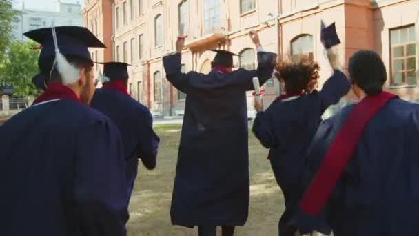 Captura Seguimiento Vista Trasera Los Estudiantes Con Sombreros Vestidos Universitarios — Vídeos de Stock