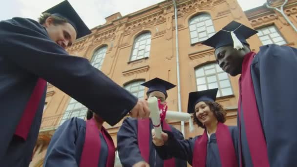 Niski Kąt Widzenia Studentów Sukniach Kapeluszach Podnoszących Dyplomy Ceremonii Ukończenia — Wideo stockowe