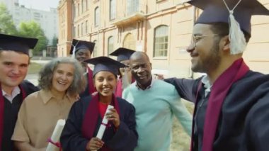 Mezuniyet töreninden sonra ailesi ve arkadaşlarıyla selfie çekerken elinde cihaz olan genç bir öğrencinin görüntüsü.