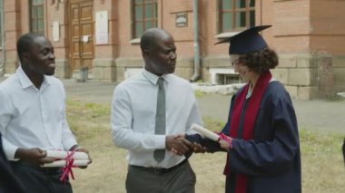 Orta boy erkek Afrikalı Amerikalı öğretmen ve genç asistanının lisansüstü öğrencilerine diploma verirken.