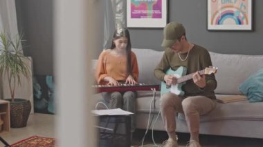 Gitar çalan genç bir adam ve evinde müzik yaparken sentezleyici çalan bir kız.