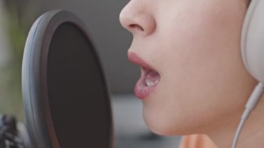 Ev stüdyosunda müzik kaydederken kulaklıklı genç bir kızın gözleri kapalı mikrofonda şarkı söylediği yakın çekim.