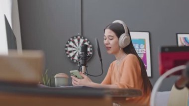 Ev müziği stüdyosunda şarkı söylerken kulaklıklı kız akıllı telefondan şarkı söylüyor ve mikrofona şarkı söylüyor.