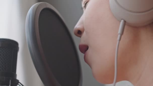 ホームスタジオで歌を録音しながらヘッドフォンで歌う若い女性歌手のクローズアップショット — ストック動画