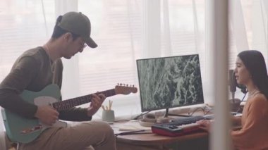 Genç müzik grubunun, evde, kulaklıkla konuşan bir kızı sentezleyiciyle konuşurken dikey çekimleri.