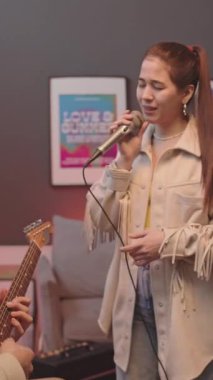 Genç yetenekli kadının mikrofon tutarken ve erkek arkadaşı olarak şarkı söylerken ev müziği stüdyosunda dikey zoom çekimi.
