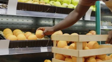 Tanımlanamayan siyah erkek süpermarket çalışanının sabah ürünlerini sergilerken olgun portakalları rafa koyduğu görüntüler.