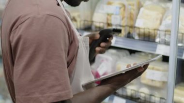 Tanımlanamayan siyah erkek süpermarket çalışanının barkod tarayıcısı ve dijital tablet kullanarak dondurulmuş ürünleri denetlerken görüntüsü.